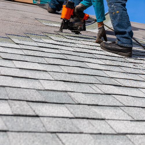 Roofers installing gray shingles with a nail gun on a sloped roof