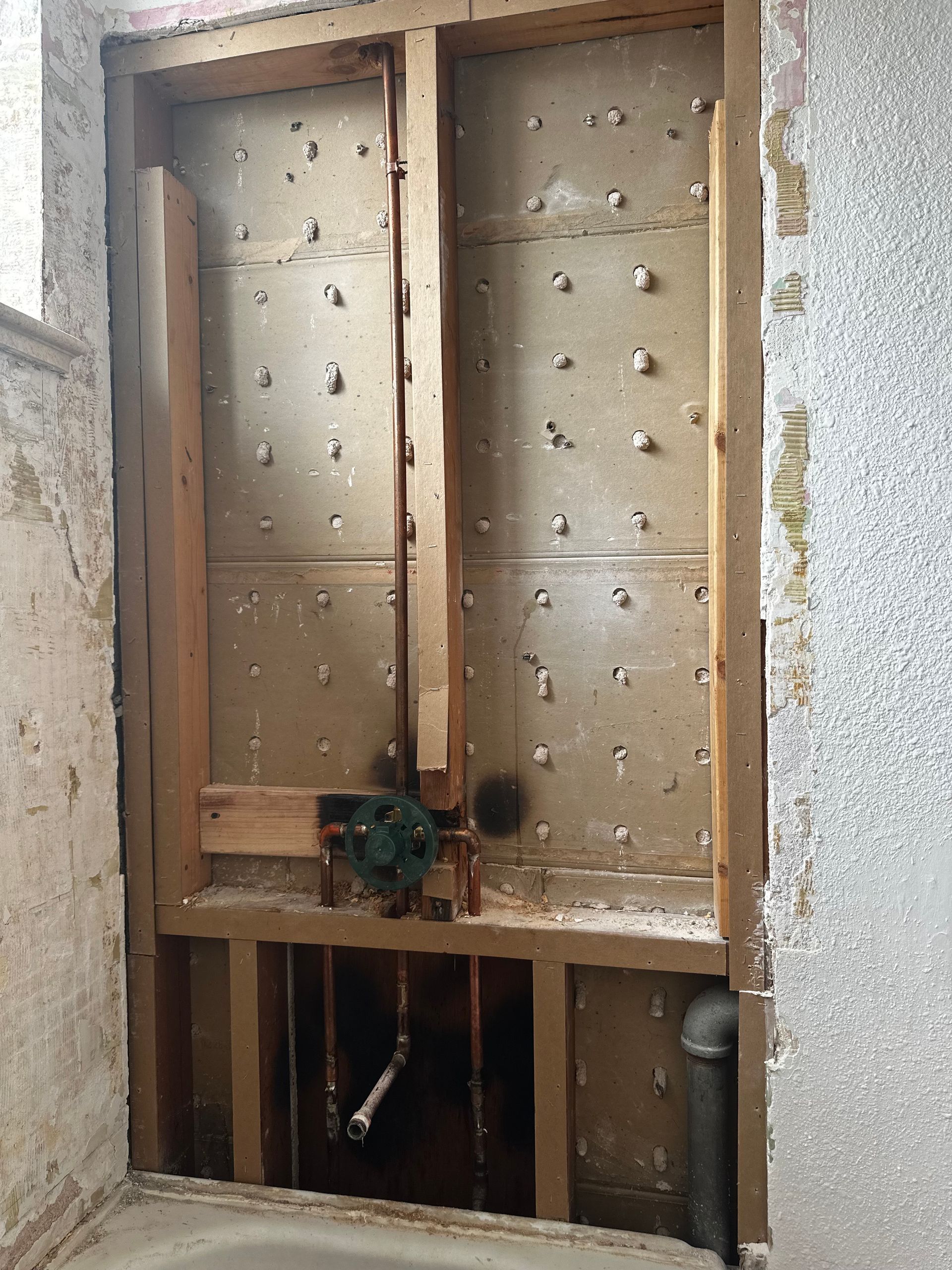 A bathroom with a hole in the wall and pipes coming out of it.