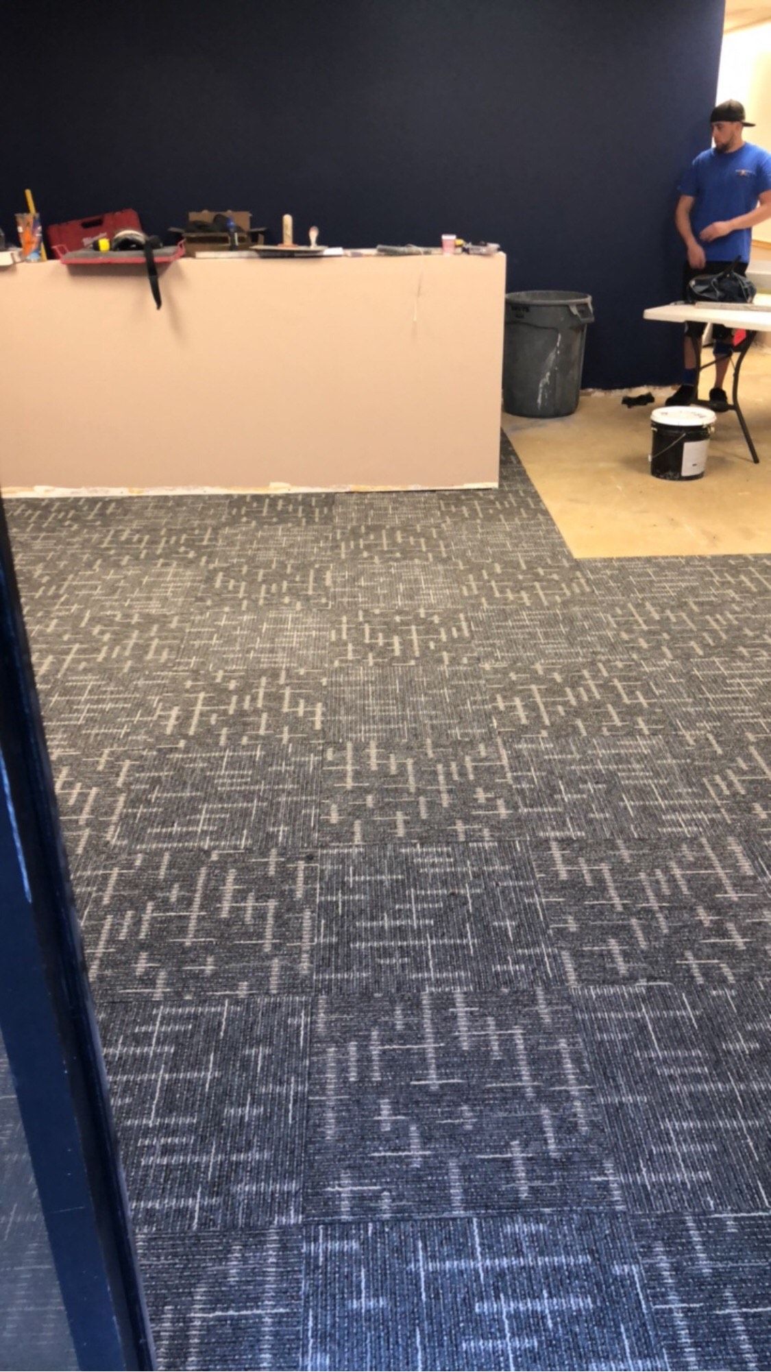 A man is standing next to a table in a room with a carpeted floor.
