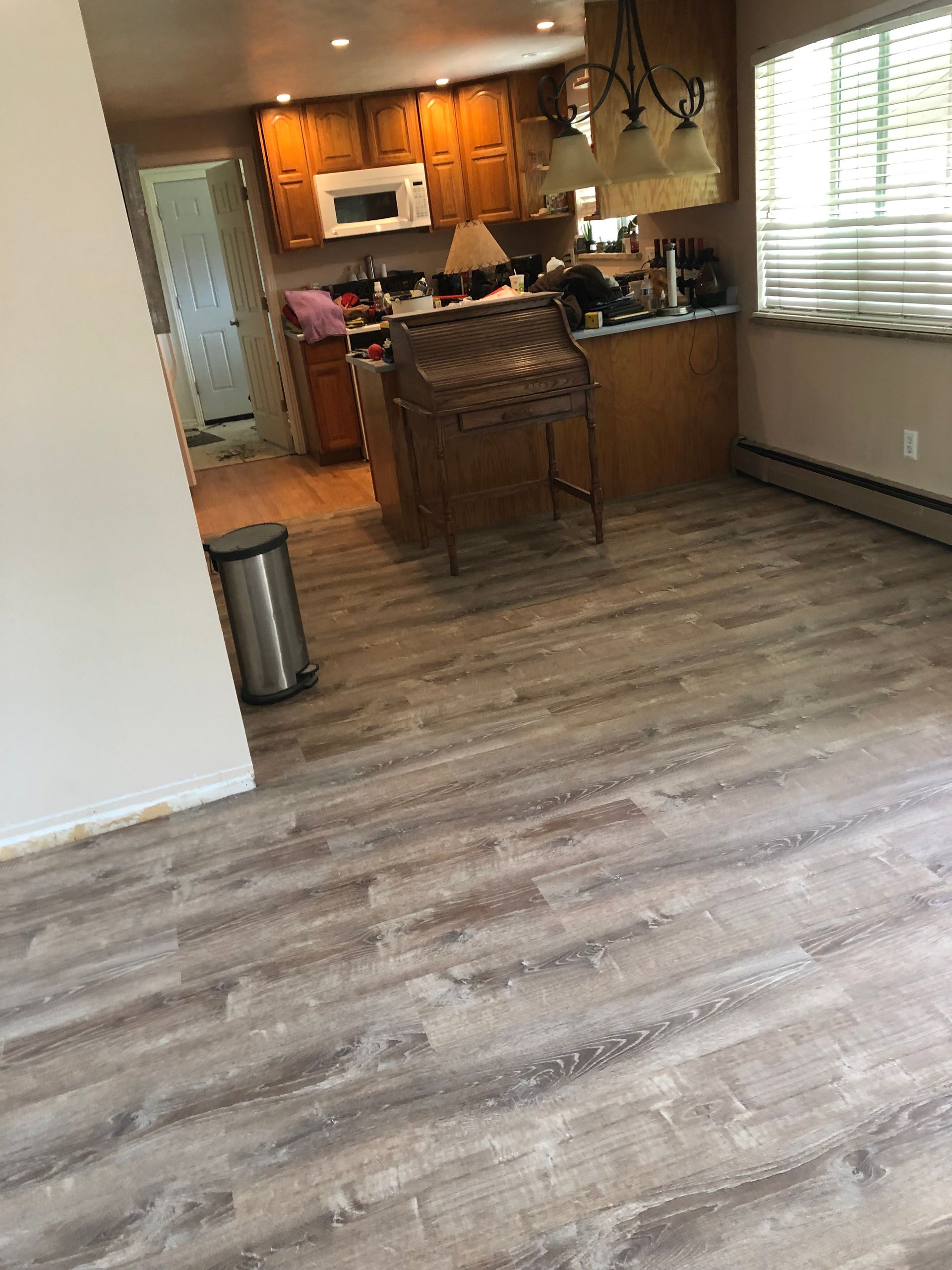 A living room with a wooden floor and a kitchen in the background.