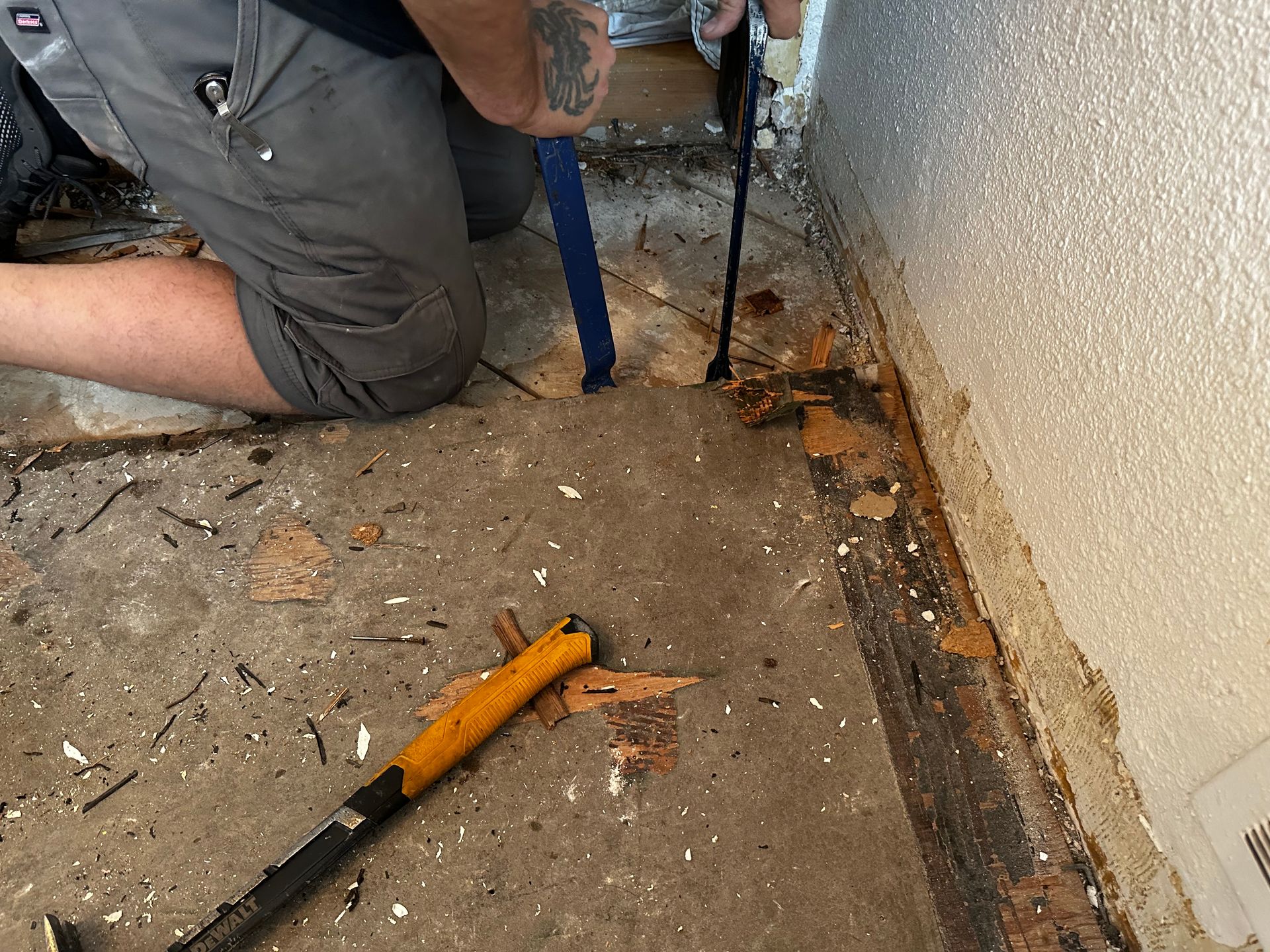 A man is kneeling down on the floor holding a tool. Getting ready to replace tile flooring