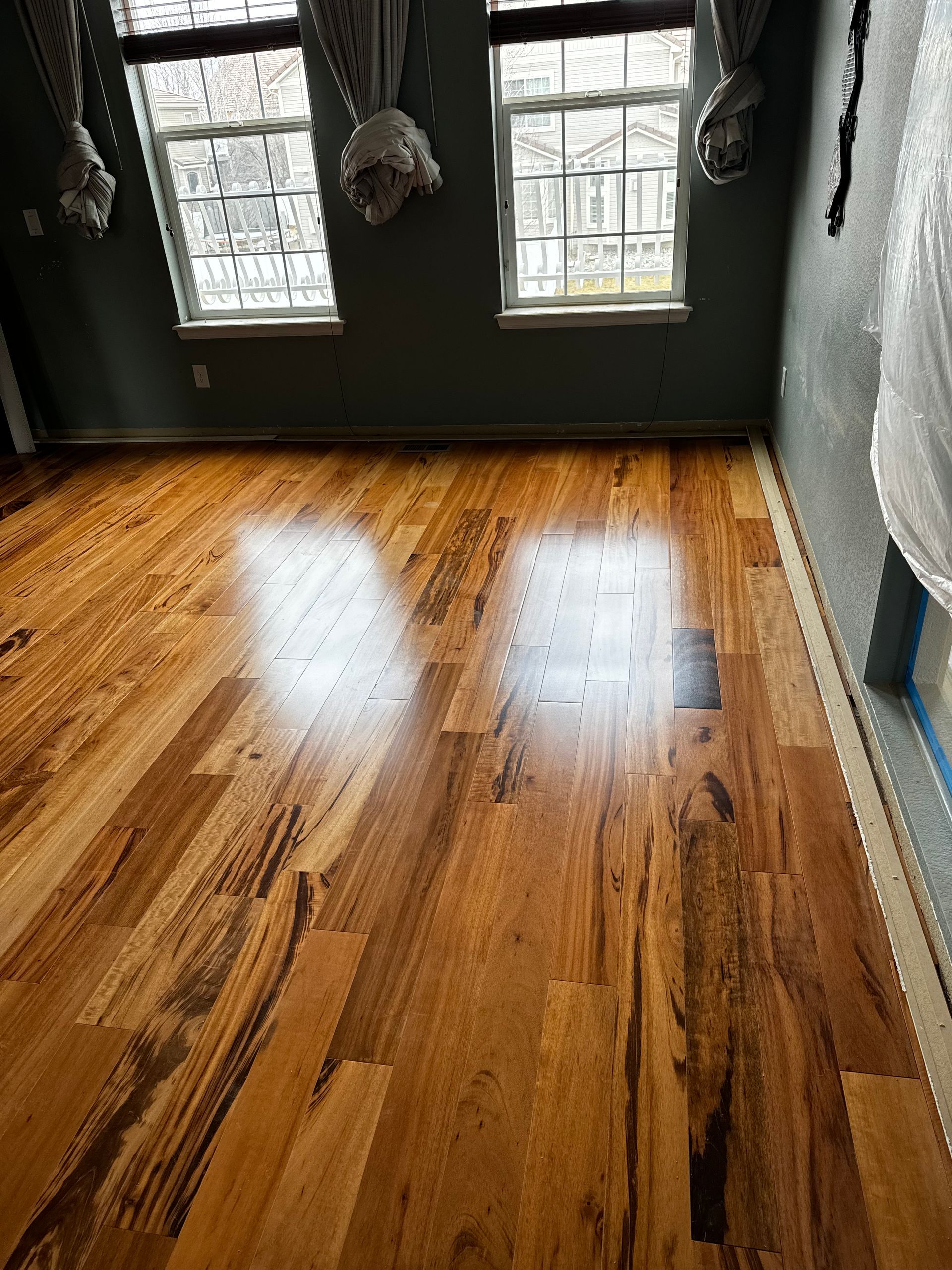 A living room with brand new hardwood floors and three new windows.