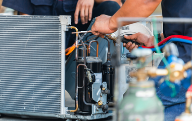 A man is working on an air conditioner with a wrench.