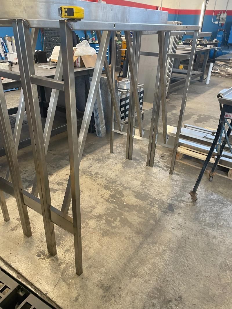 Una fila di cavalletti in acciaio inossidabile è appoggiata su un pavimento di cemento in una fabbrica.