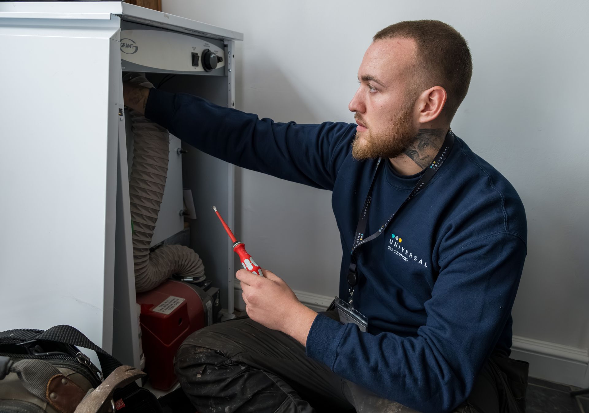 Man in blue sweater, with beard, fixing white appliance with screwdriver; indoors.