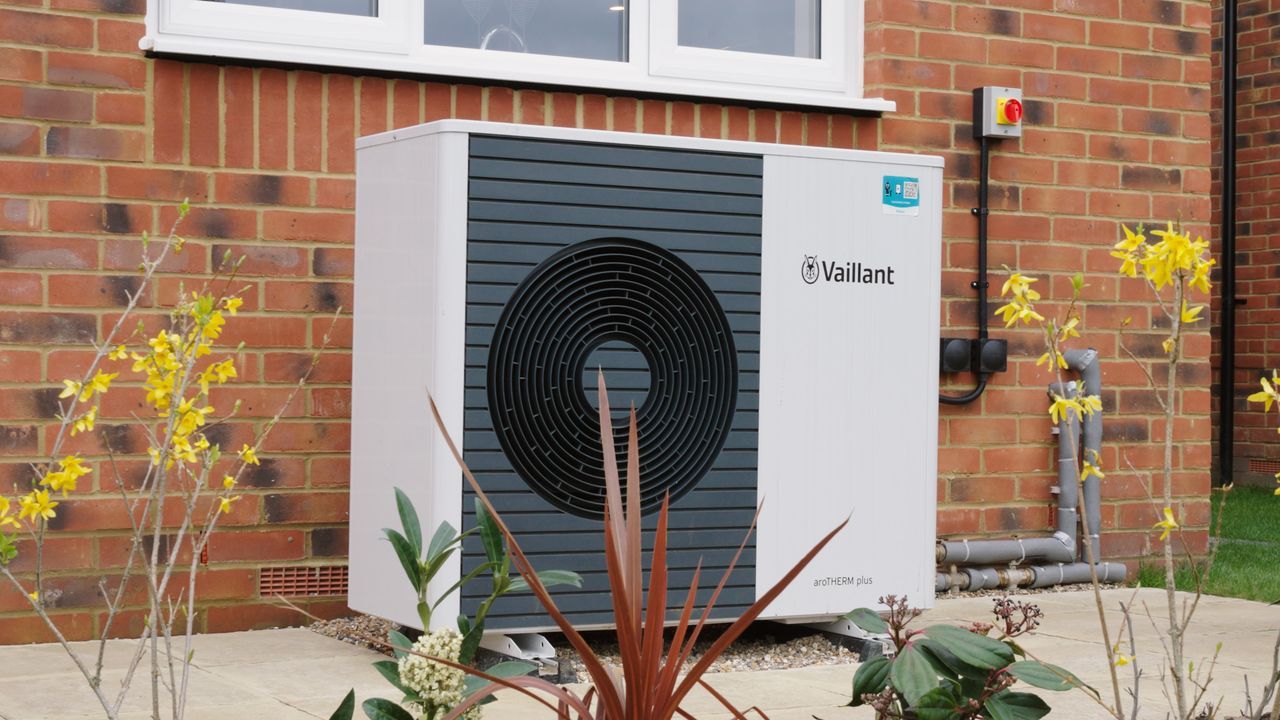 Heat pump unit installed next to a brick house, surrounded by plants.