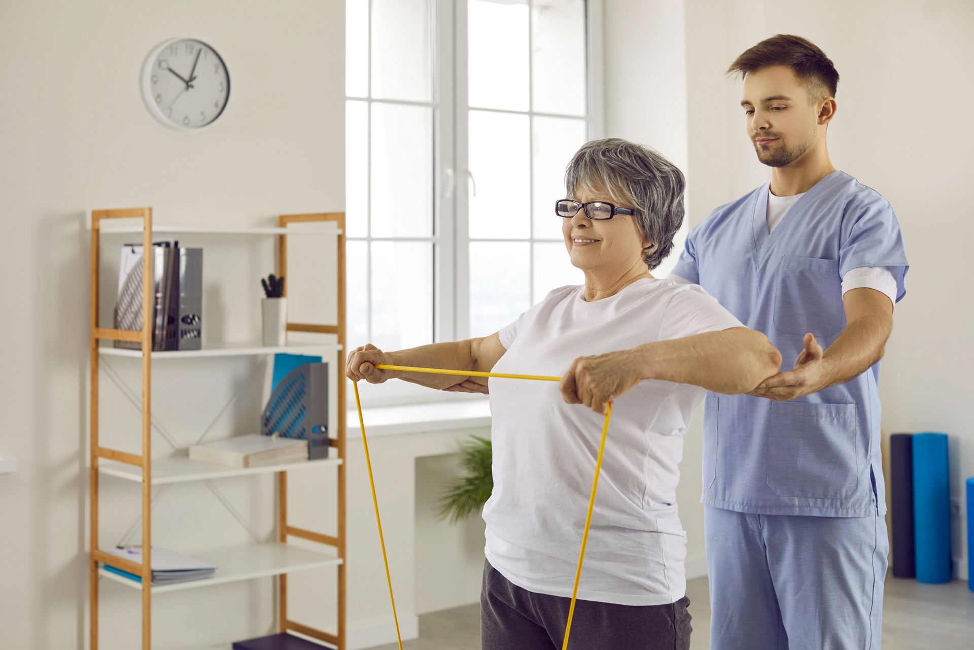 A senior lady is doing exercises with rubber, with a physiotherapist standing behind and helping her. A senior lady is doing exercises with rubber, with a physiotherapist standing behind and helping her.