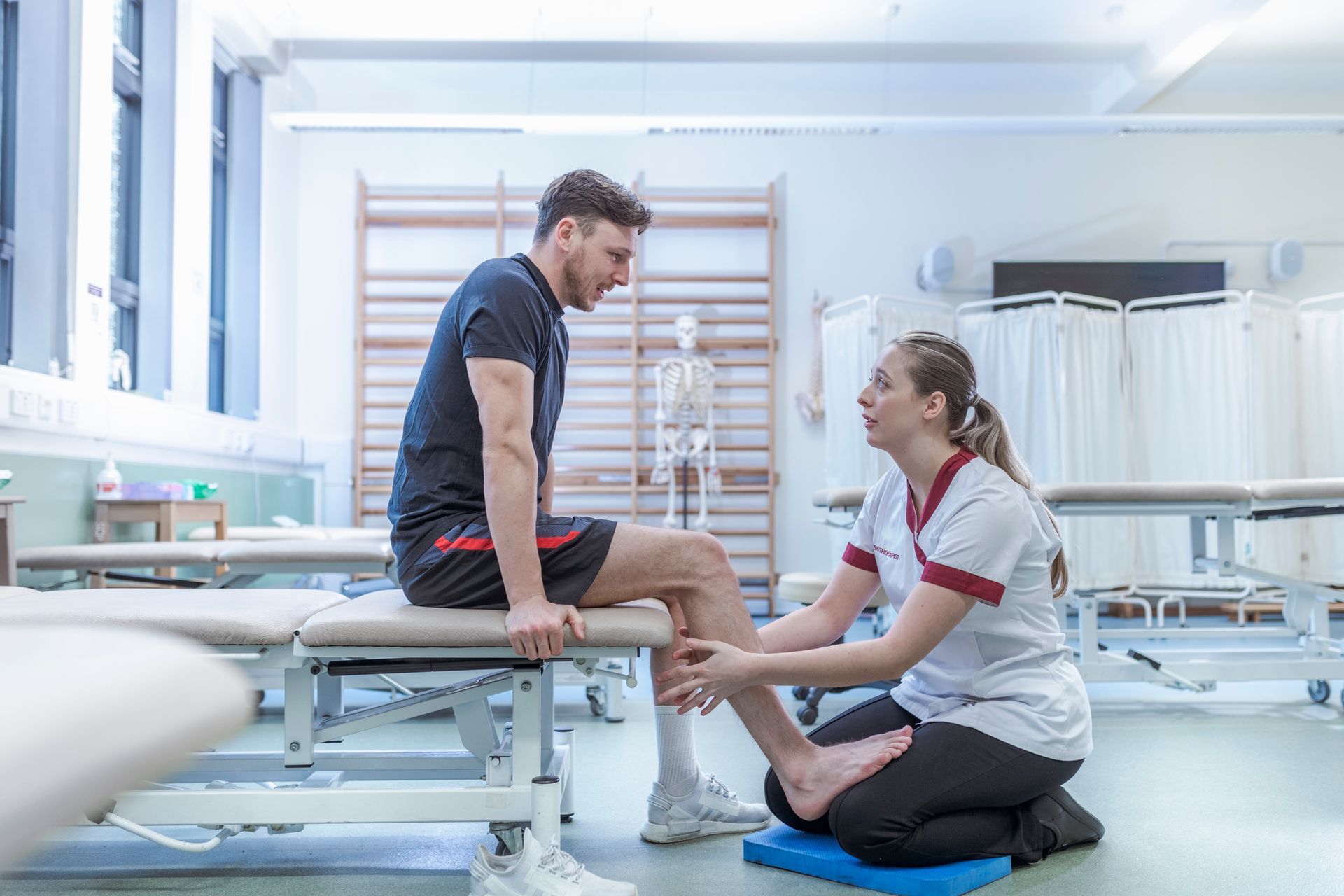 A female blonde-haired physiotherapist with a white male patient in a hospital