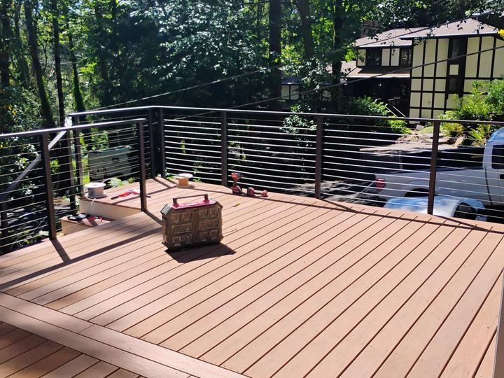 Wooden deck with black railing in a wooded backyard, with a wicker basket on the floor.