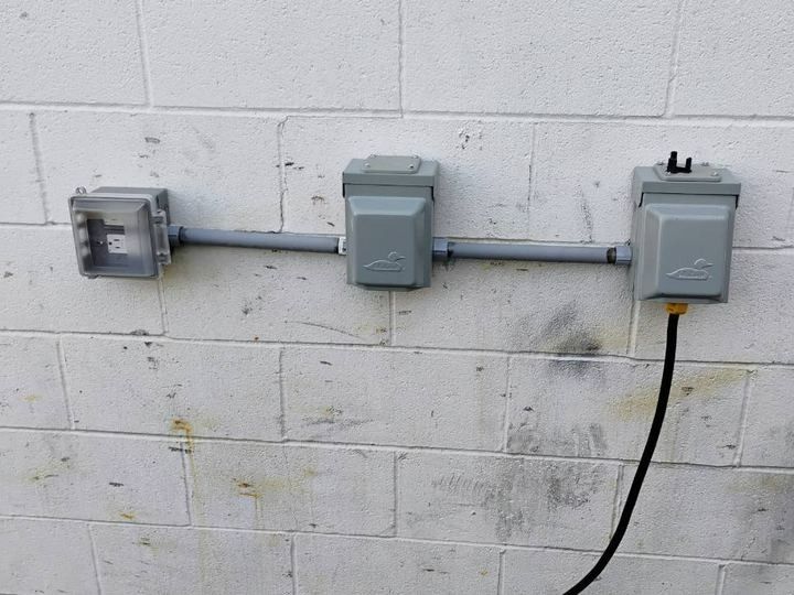 Electrical boxes and conduit mounted on a white cinder block wall, with a black cable hanging down on the right.