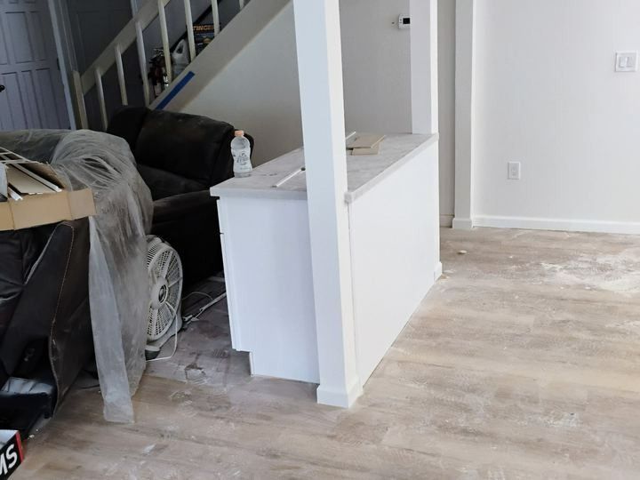 Empty living room with staircase, white walls, and light wood flooring during renovation