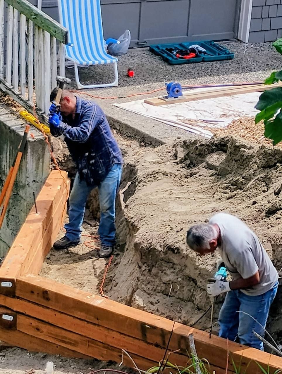 Two workers installing wooden forms and digging a backyard trench at a construction site.