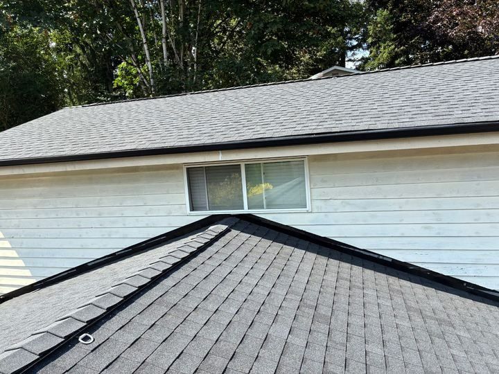 Roof valley meeting white house siding and a small window, with dark shingles in the foreground.
