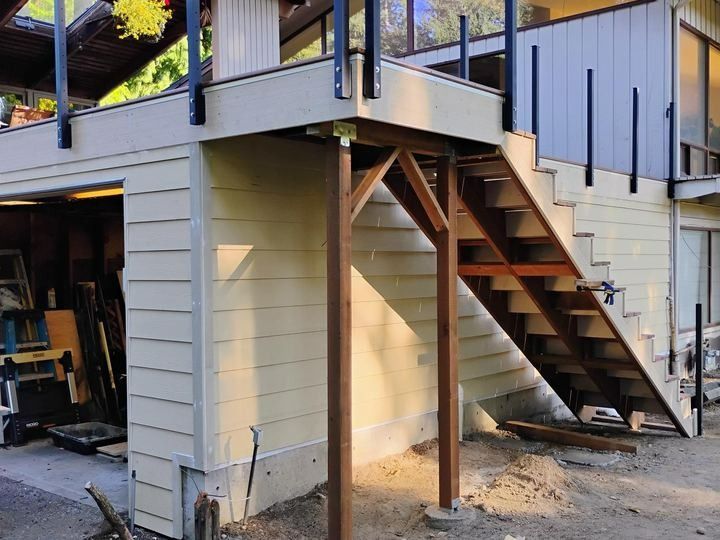 Exterior staircase under a raised deck beside a beige house with white railings and support posts