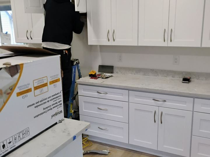 Kitchen with white cabinets and counters; a person stands on a ladder near the upper cabinets.