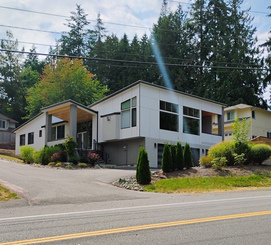 White house on a sloped street surrounded by trees, with a sunbeam and utility lines overhead.