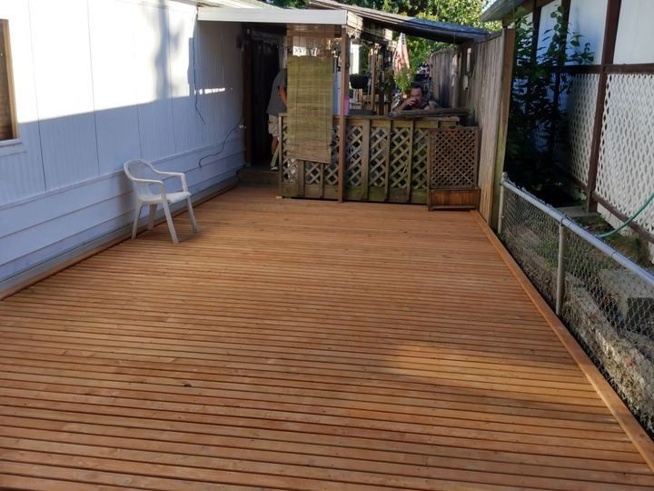 Wooden deck beside a white house, with a chair, covered seating area, and chain-link fence.
