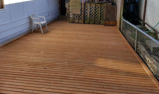 Wooden deck patio with a white chair, lattice planters, and a chain-link fence along the side