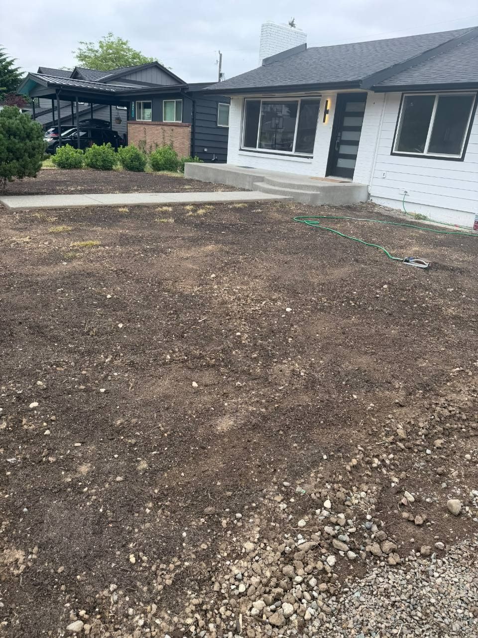 Front yard with bare soil and a small white house with black trim and a patio.