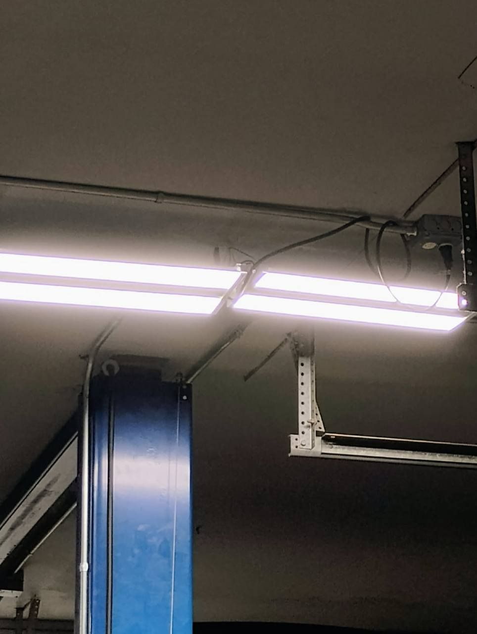 Fluorescent ceiling lights and wiring above a blue metal support in a workshop or garage ceiling