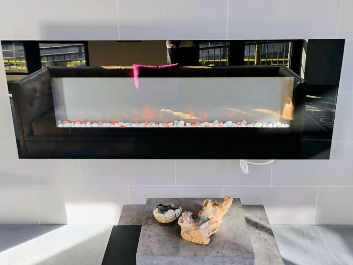 Modern black wall-mounted fireplace above a stone hearth with driftwood decor