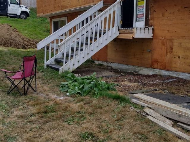 White stairs on a house under construction beside a pink folding chair and lumber in a grassy yard.