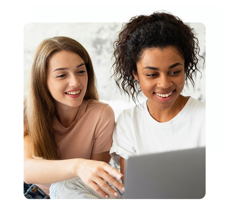 Dos mujeres están sentadas en una cama mirando una computadora portátil.