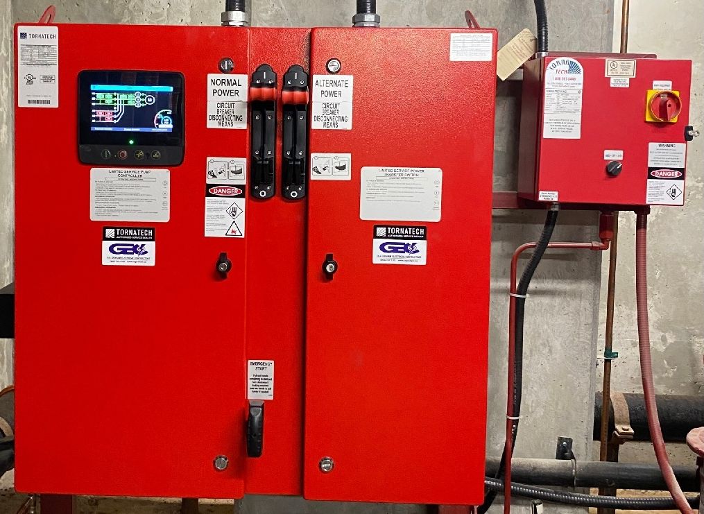 Red electrical control panels with warning labels and a small display in an industrial room