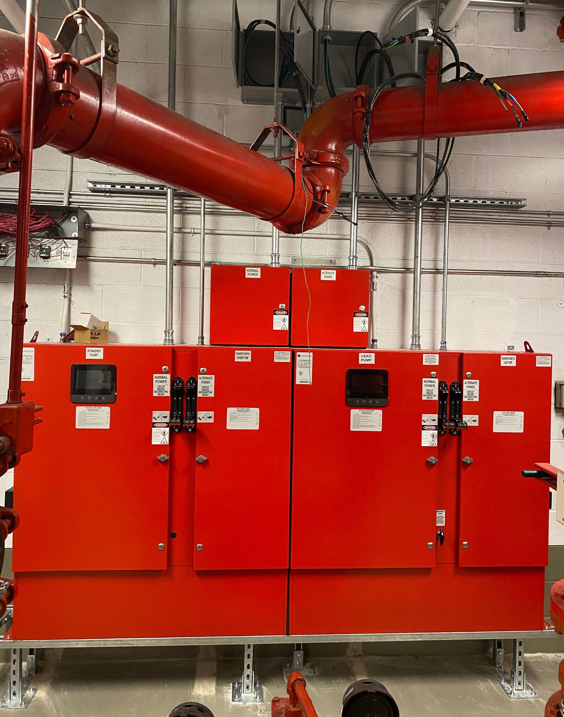 Red fire suppression control cabinets with large overhead red pipes in an industrial room
