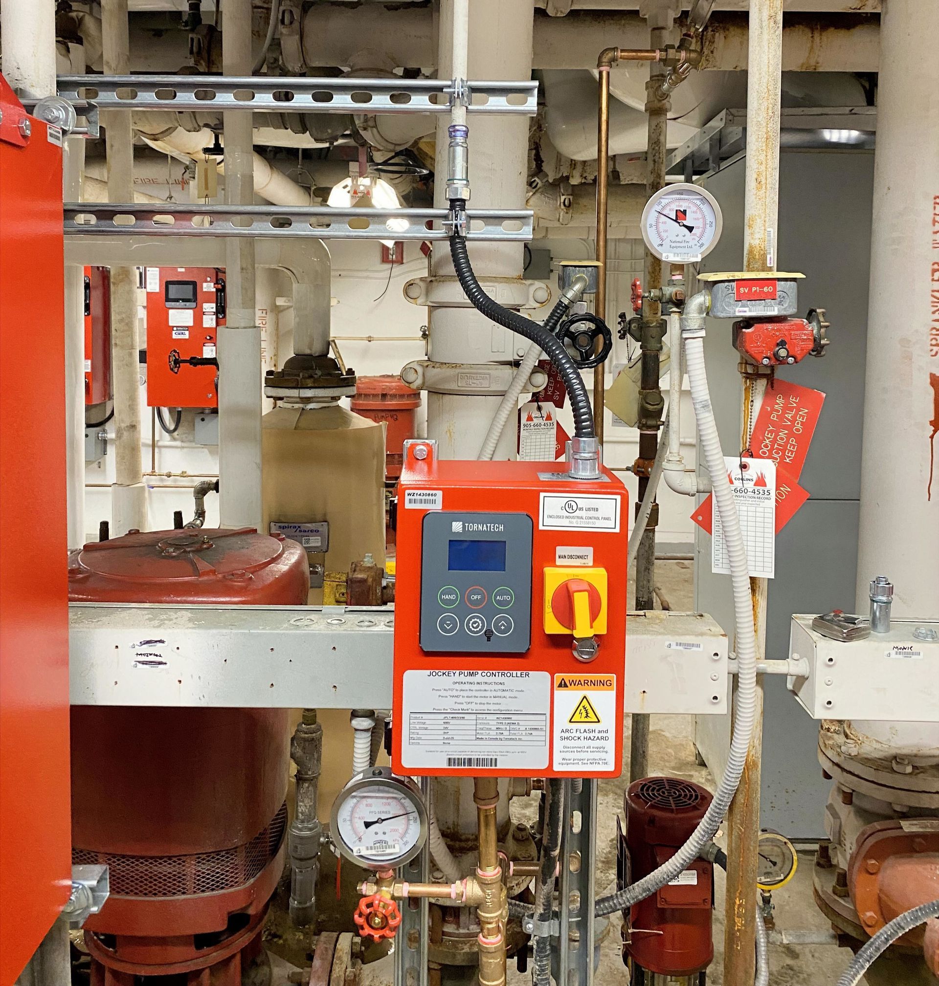 Industrial machinery with red control boxes, pipes, gauges, and valves in a factory setting