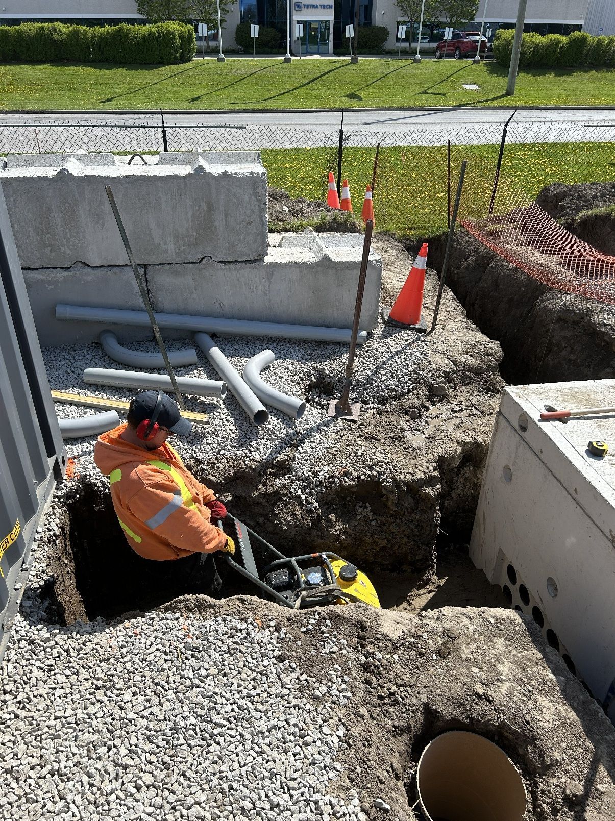 Worker in orange vest repairing a gravel-lined utility trench at a construction site.