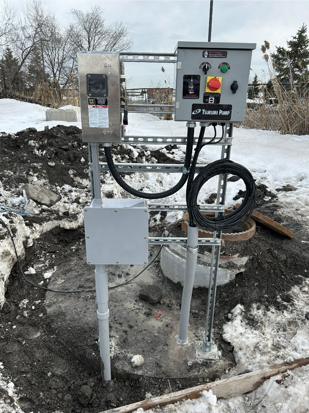 Outdoor electrical control panel with buttons and wiring mounted on posts in a snowy worksite