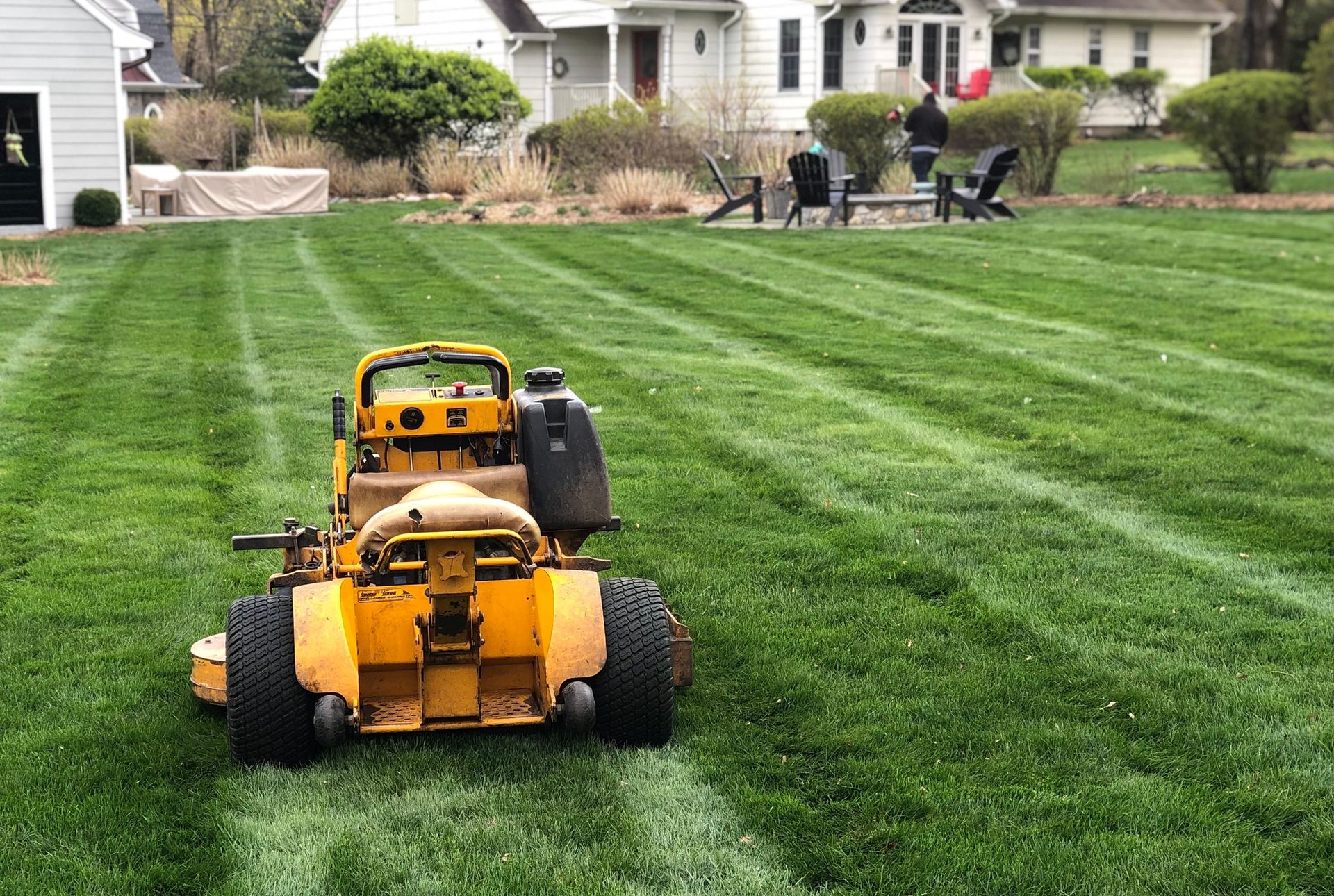 A yellow riding lawn mower sits on a freshly striped green lawn in front of a house.