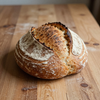 Rond, rustiek zuurdesembrood met een goudbruine, gebarsten korst op een houten tafel.