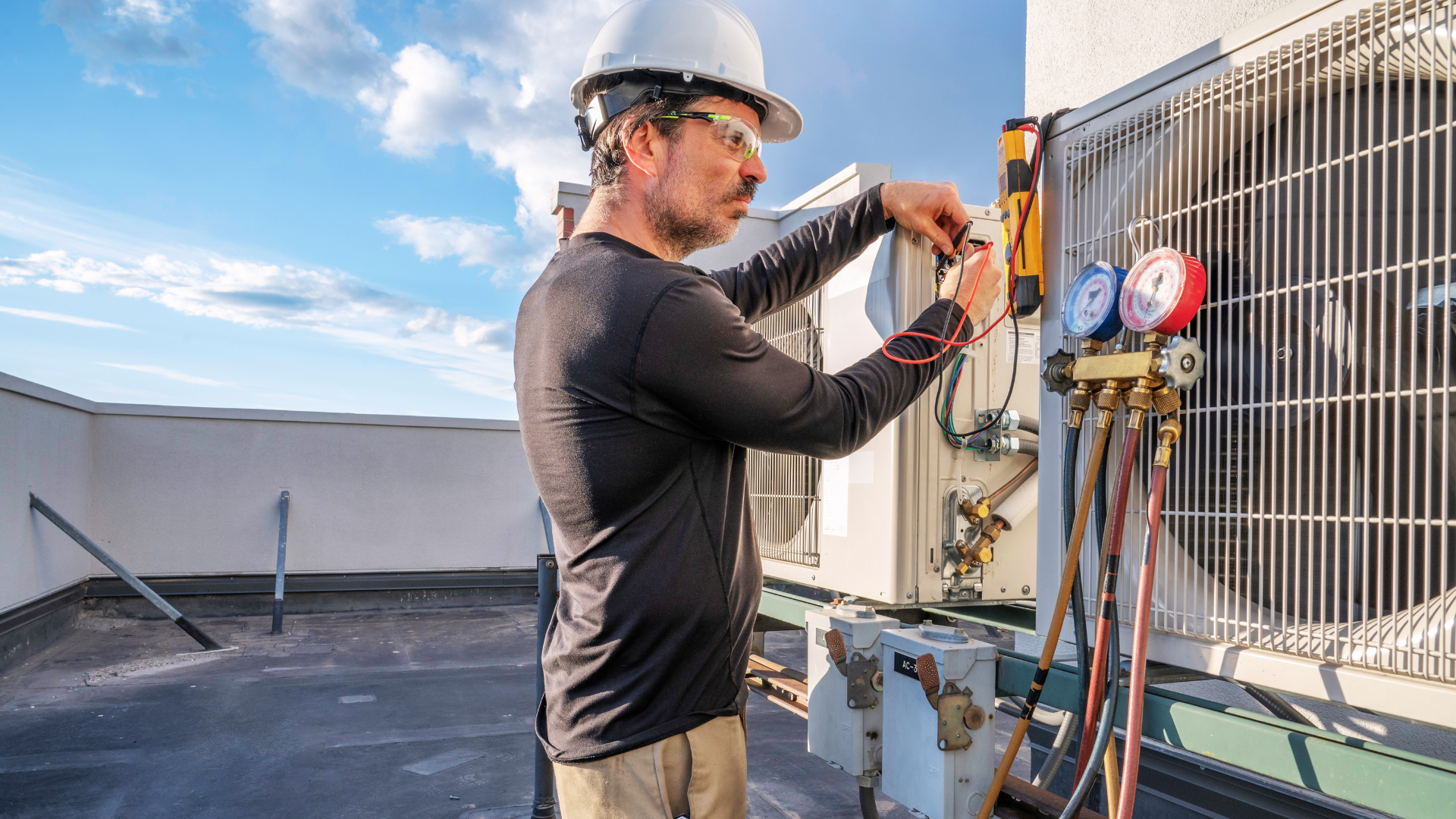A man is working on an air conditioner on the roof of a building.