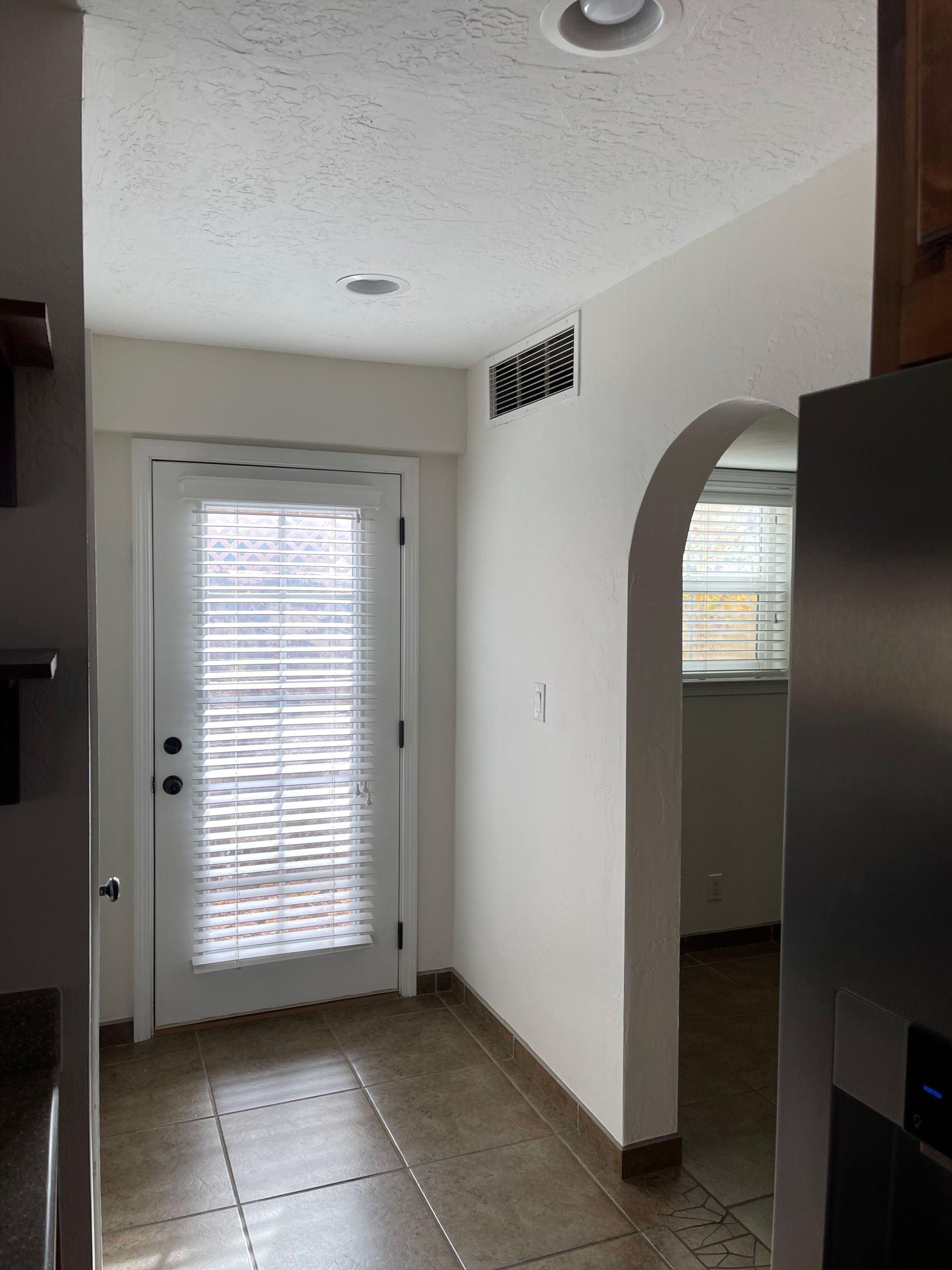 Empty white room under renovation with plastic-covered floor, open door, and sliding glass doors to the outside