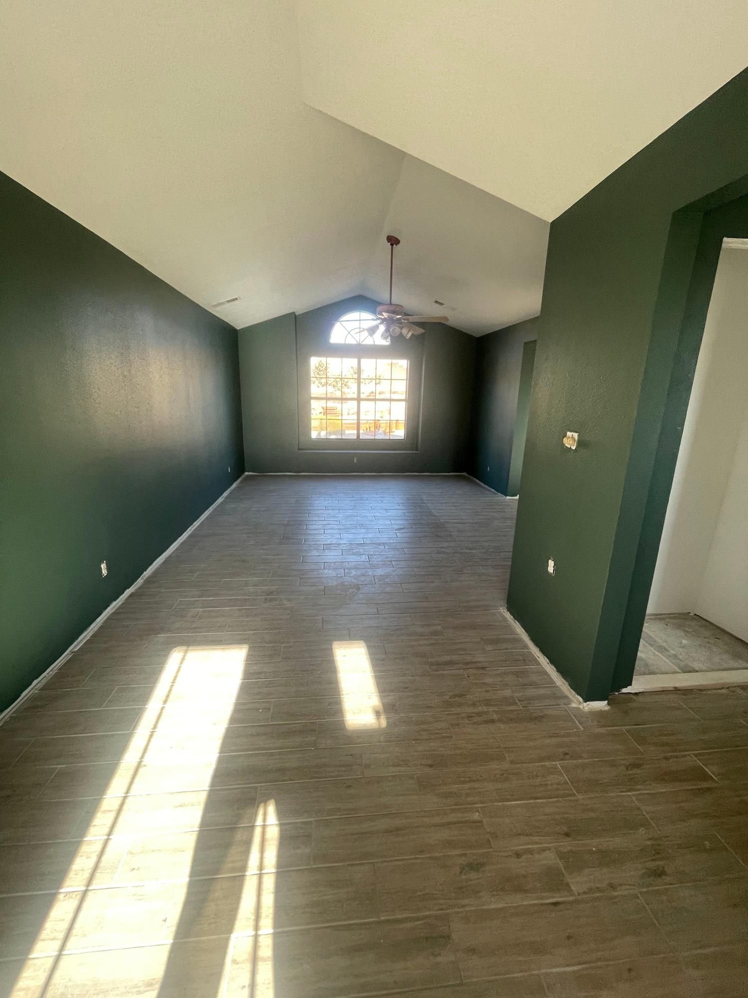 Empty room with dark green walls, wood-look floor, and sunlight streaming through a front window.