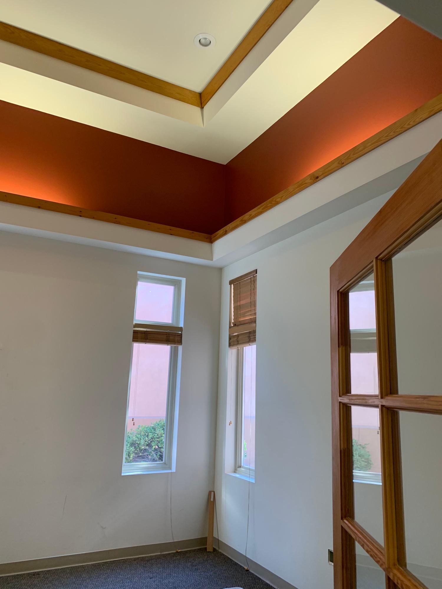 Empty room with white walls, wood trim, and a red ceiling border, seen from a corner near tall windows.