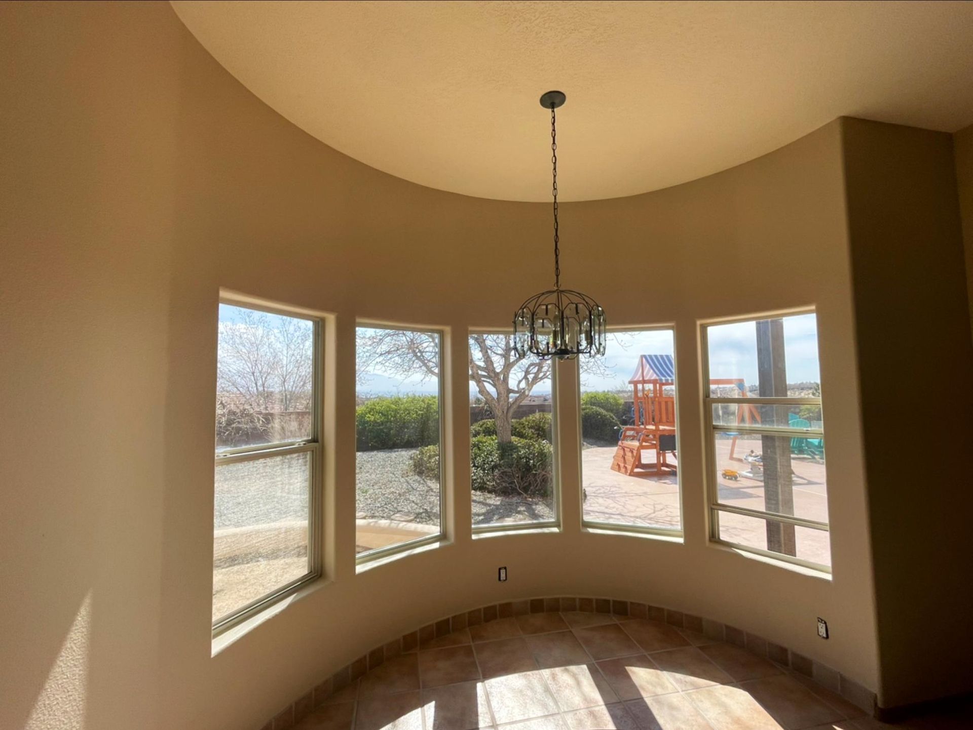 Curved bay window nook with beige walls, hanging chandelier, and patio view outside