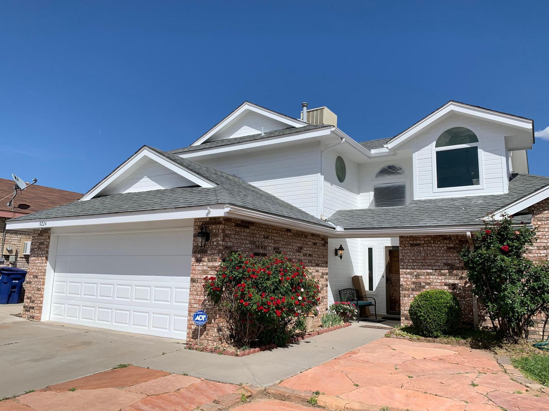White two-story suburban house with a garage, brick accents, and a clear blue sky