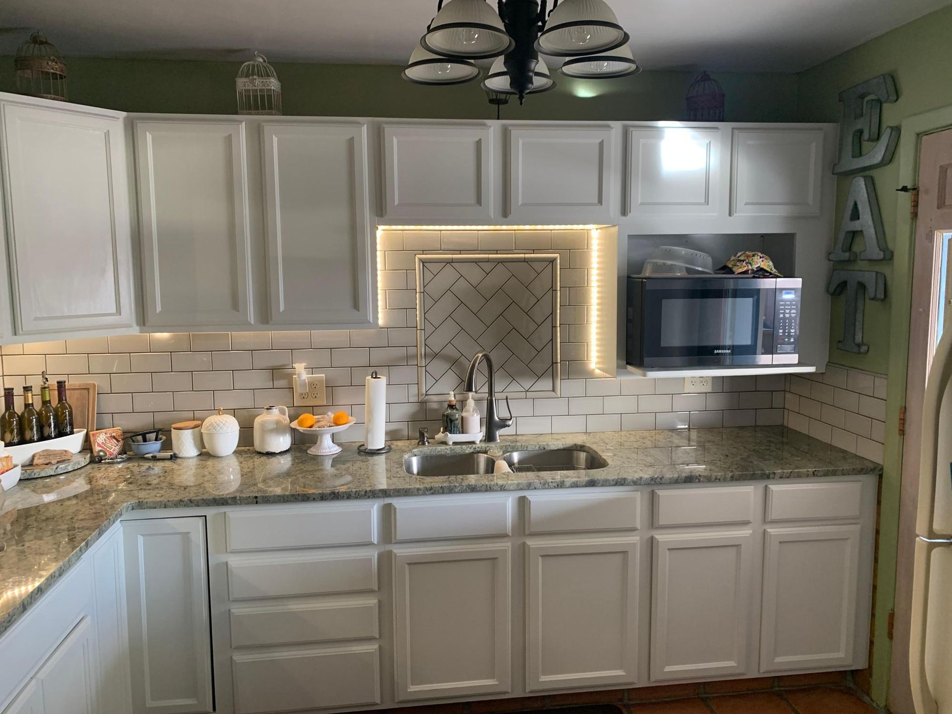 Bright kitchen with white cabinets, granite counters, and a lit herringbone tile backsplash.