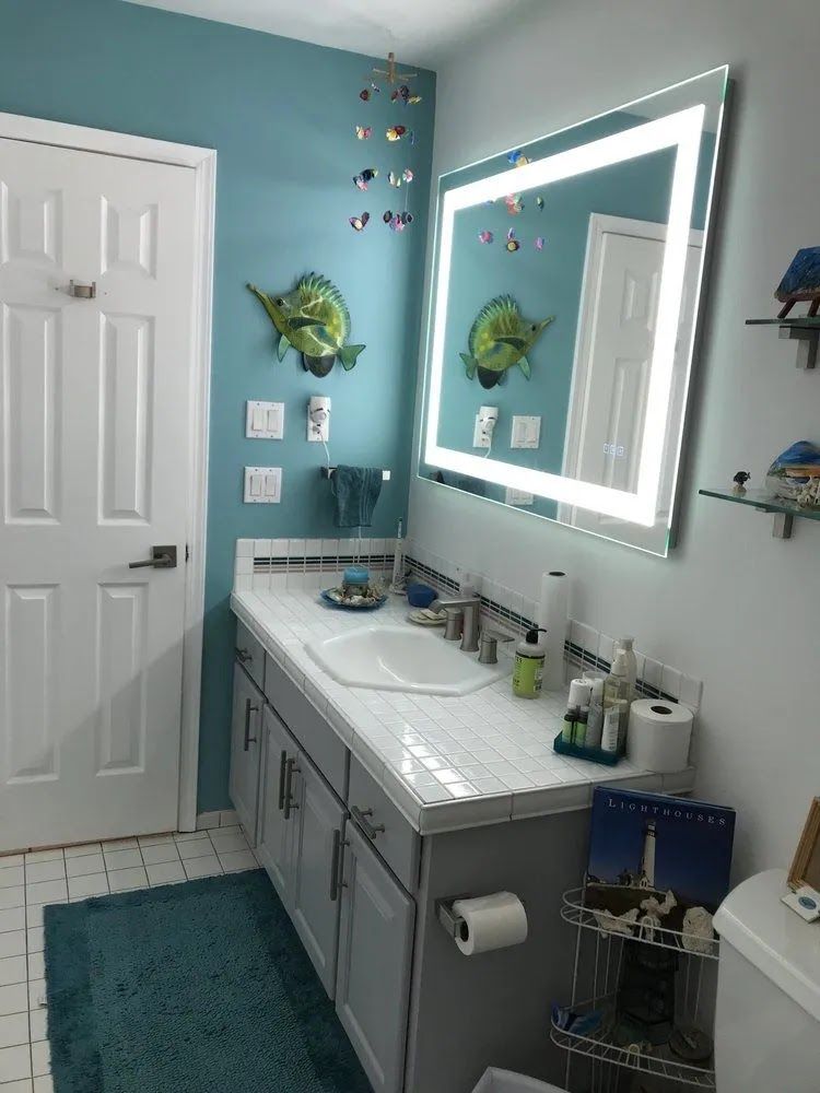 Bright teal bathroom with white vanity, large lit mirror, and tiled floor￼