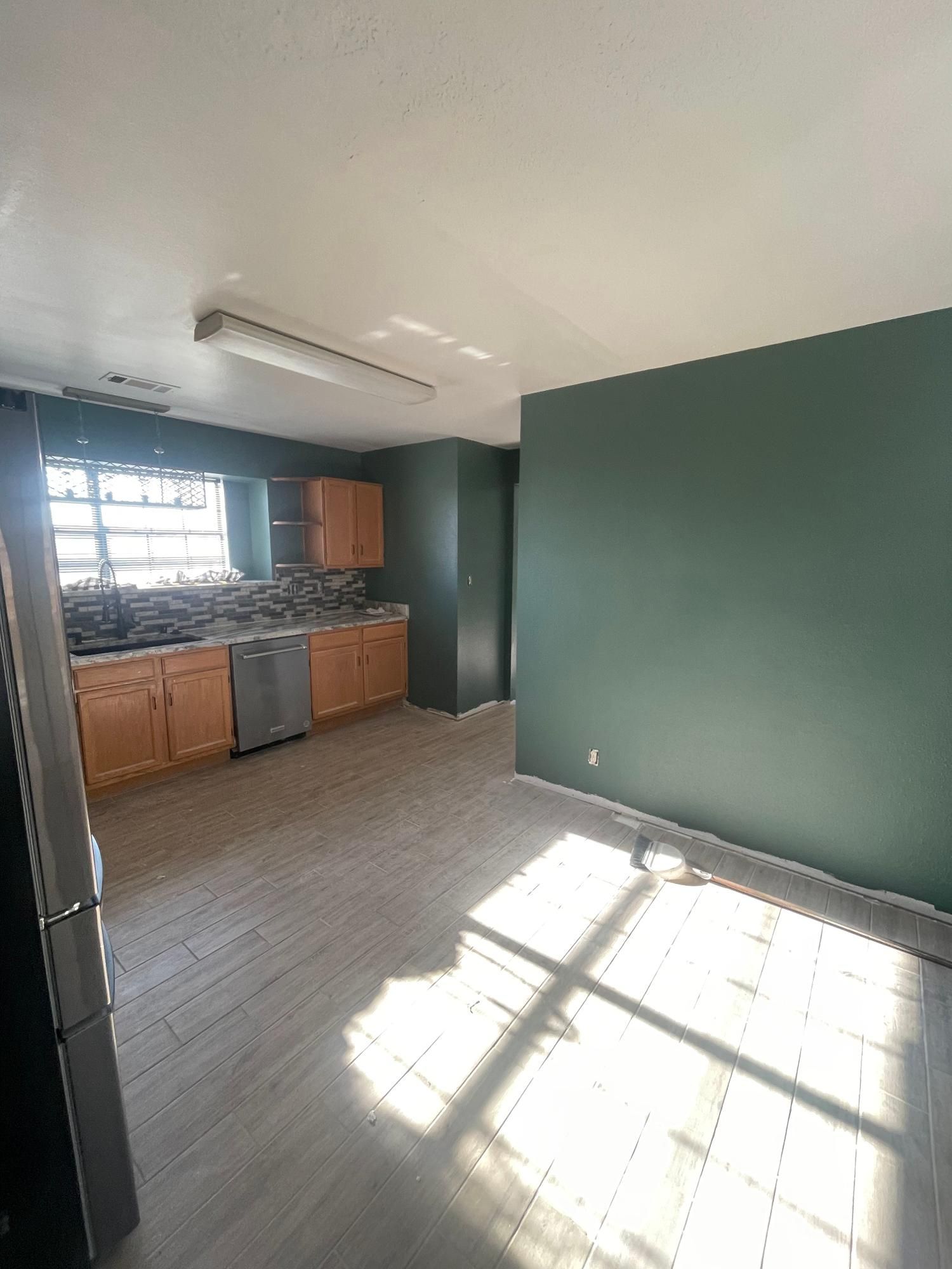 Empty kitchen with green walls, wood cabinets, tiled floor, and sunlight streaming through a window.