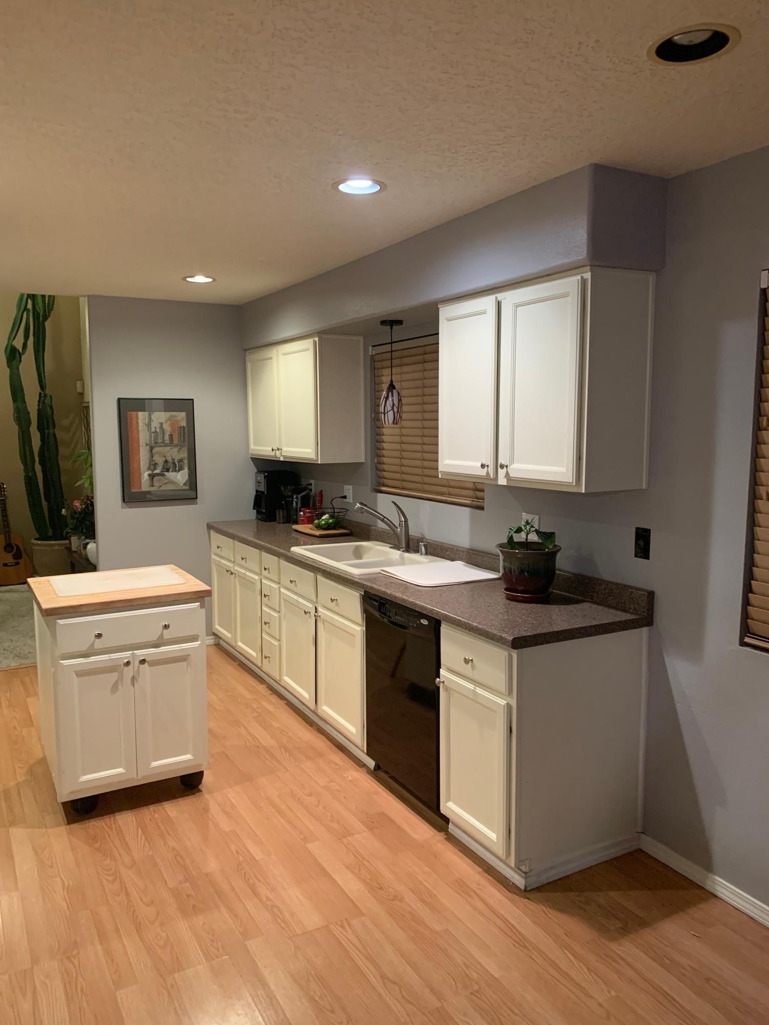 Modern kitchen with white cabinets, gray countertops, wood floors, and a small island under recessed lights