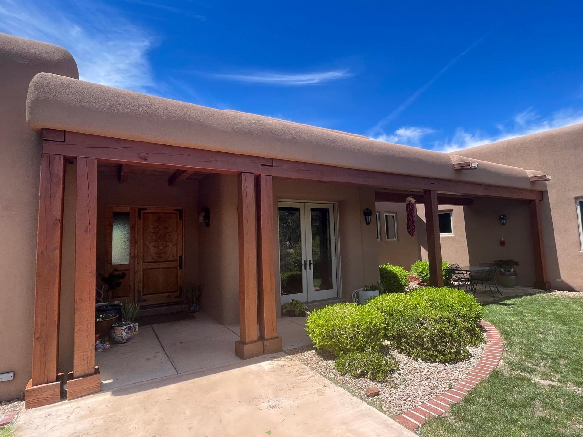 Adobe house with wooden porch posts, sliding glass doors, and a small green lawn under a clear blue sky