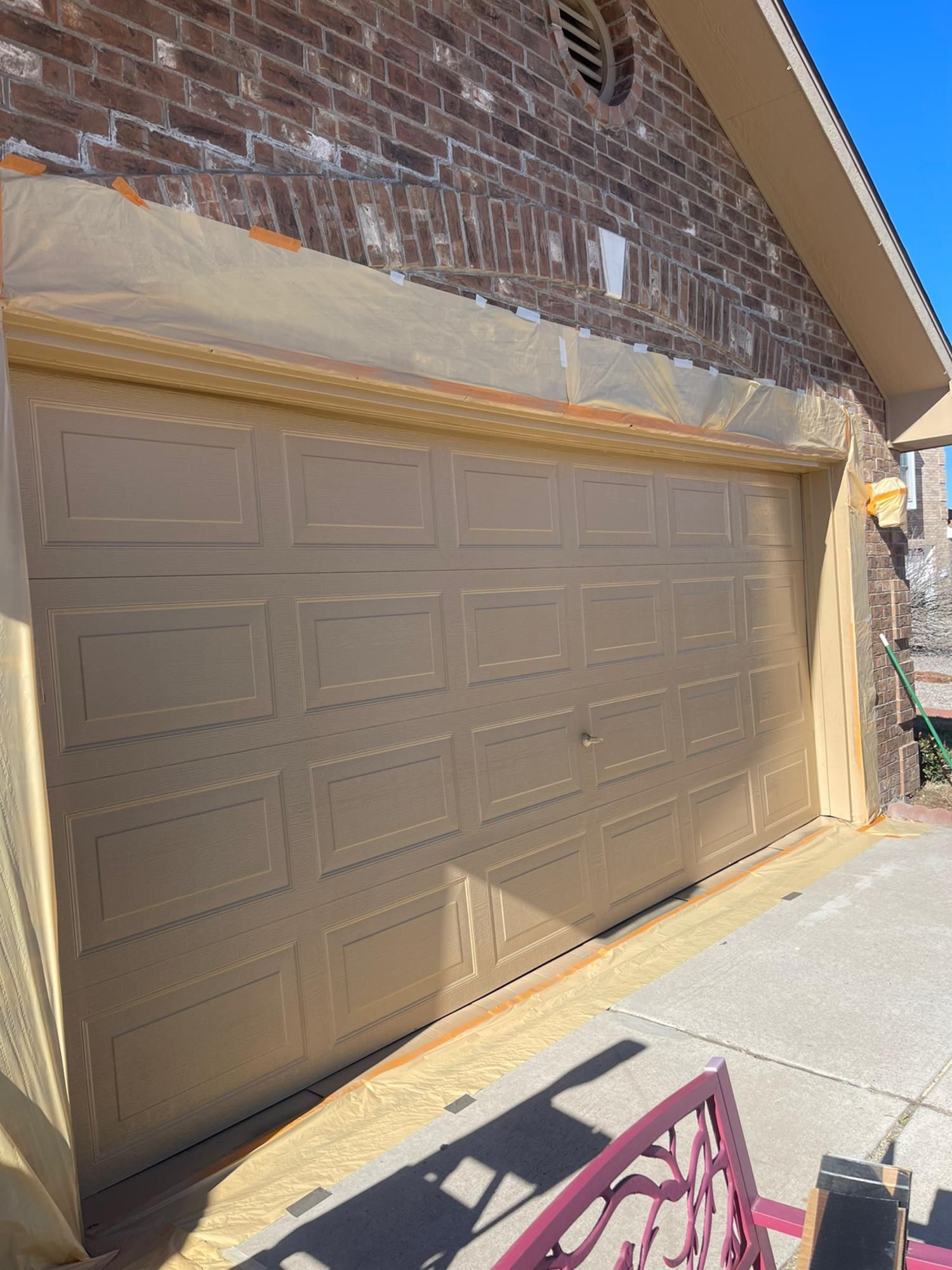 Brown garage door on a brick house with sunlight and a sidewalk in front.