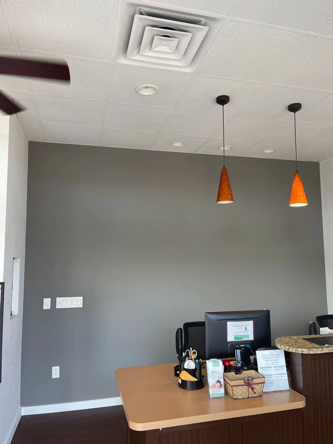 Small dining area with gray wall, pendant lights, table, and countertop with bottles and snacks.