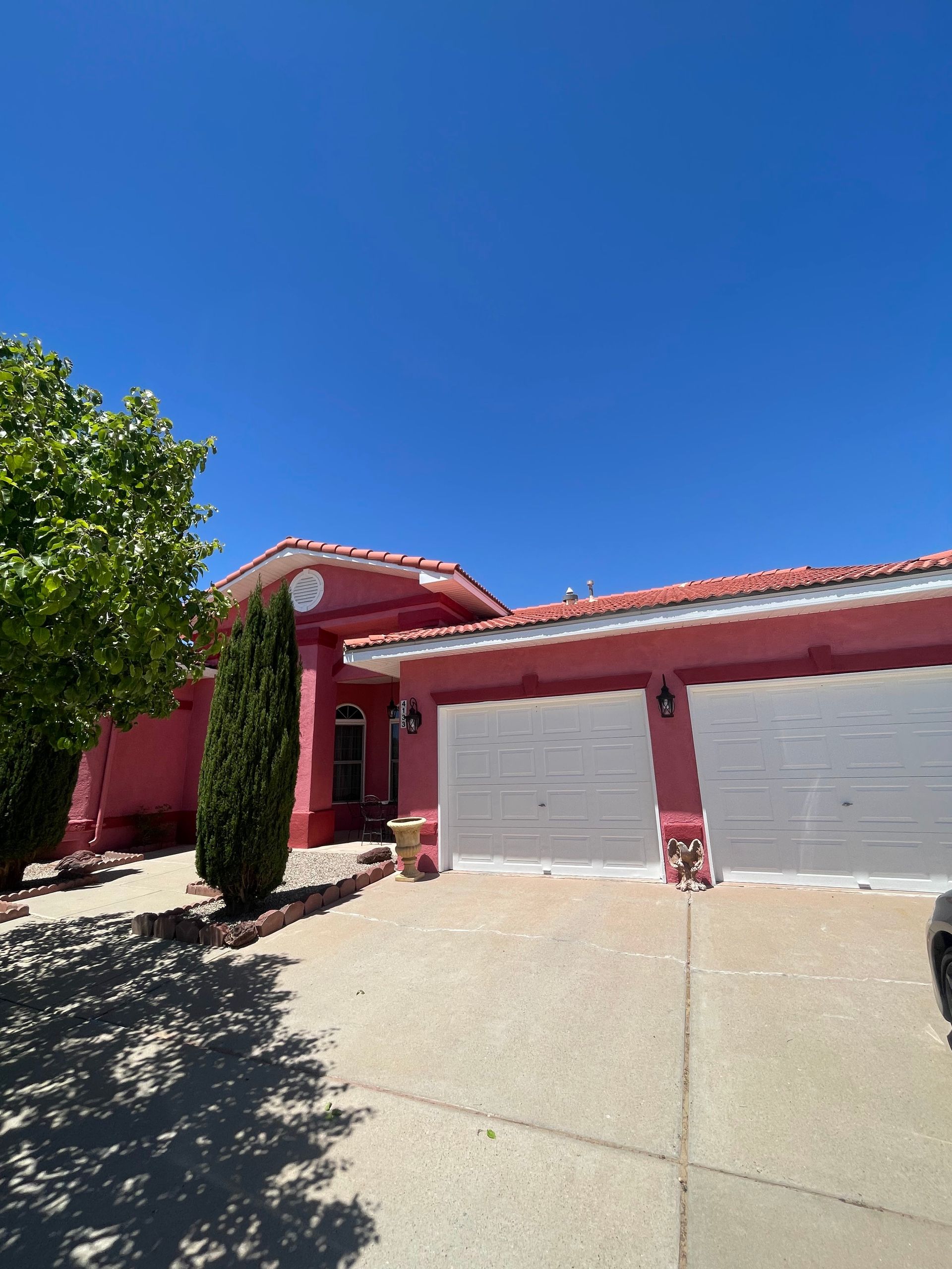 Red stucco house with a two-car garage, driveway, and clear blue sky