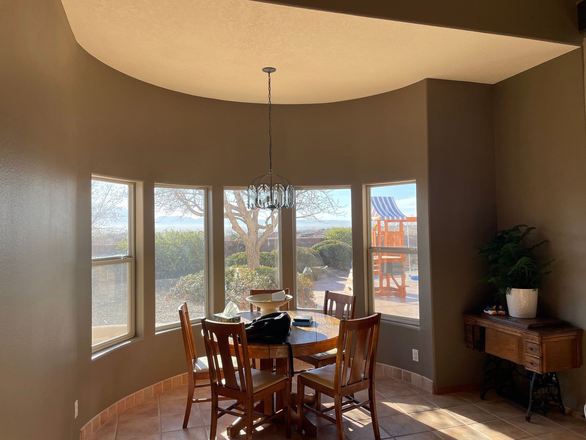 Curved dining nook with bay windows, wooden table and chairs, and a hanging light fixture.