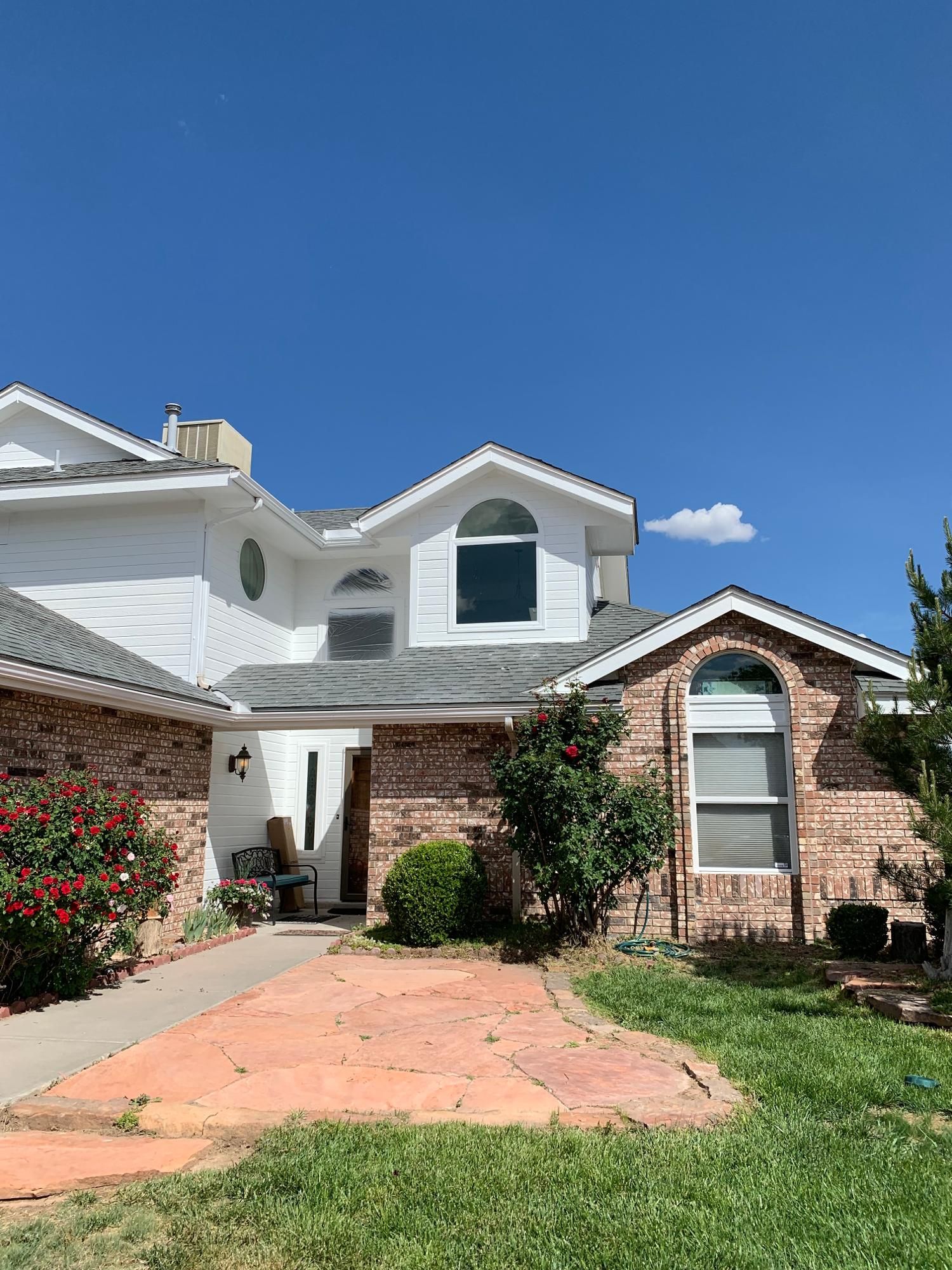 Two-story white and brick suburban house with a front walkway, lawn, and clear blue sky